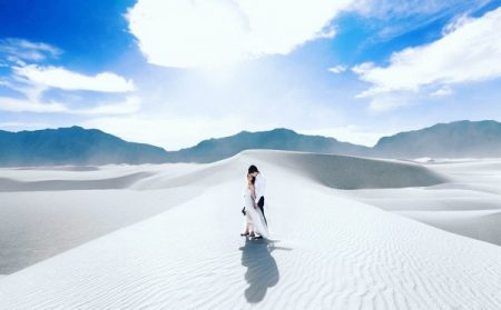 Bride and groom standing on white sand of desert with bright blue sky - Picture by Clane Gessel Photography
