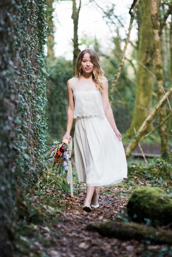 Bride holding out dress as she walks through woods