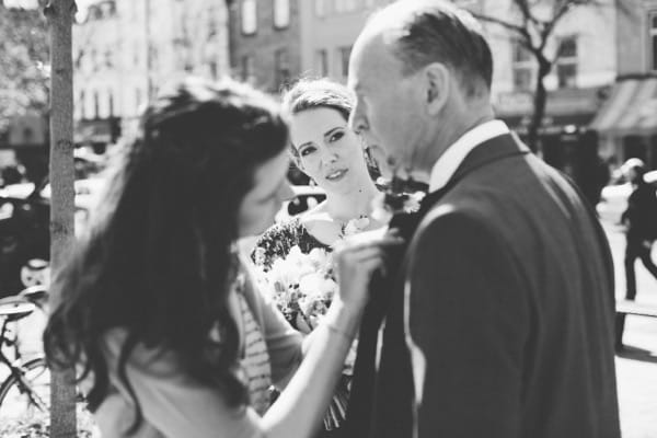 Bride watching as father has his buttonhole attached