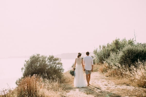 Bohemian bride and groom walking on beach in Spain