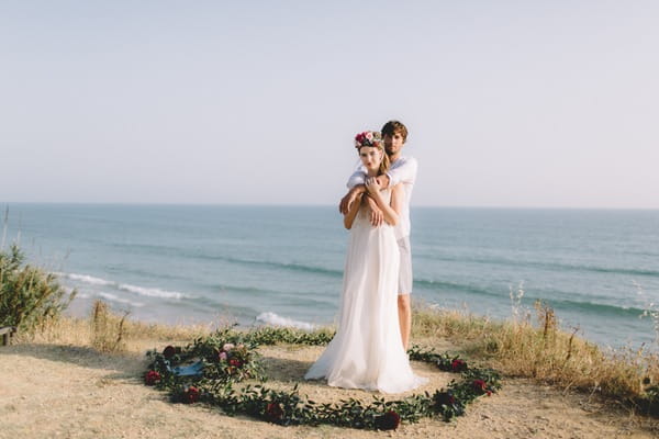 Bride and groom standing in circle of flowers on beach