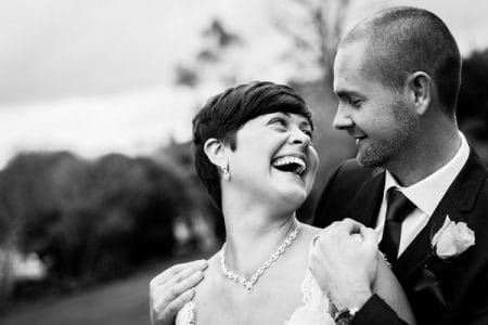 Bride looking over shoulder to smile at groom standing behind her - Picture by Joan Jellett