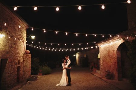 Bride and groom standing in courtyard at night with strings of light bulbs overhead - Picture by Paul Fuller Photography