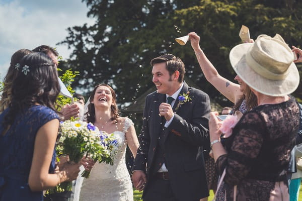 Bride and groom laughing as confetti is thrown over them