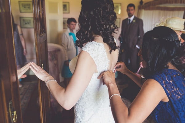 Lady doing up back of bride's wedding dress