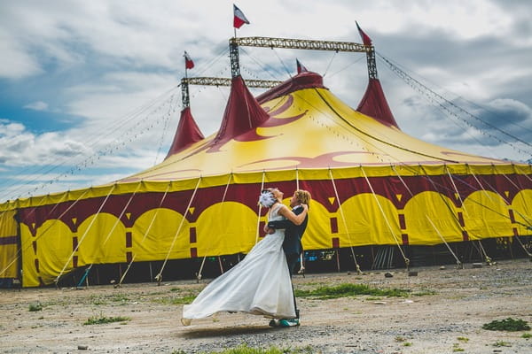 Groom lifting bride in front of circus tent