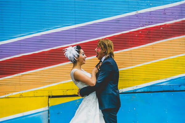 Bride and clown face groom in front of colourful wall