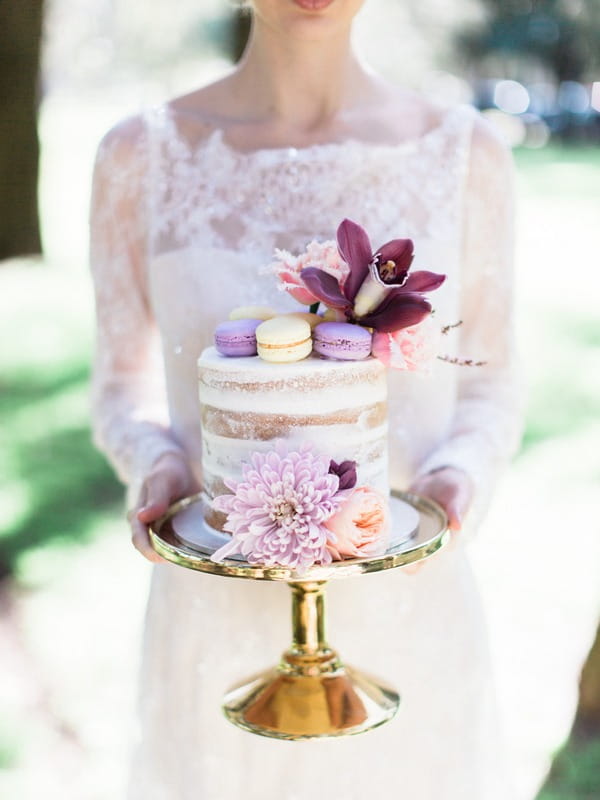 Bohemian bride holding wedding cake with flower and macaroons