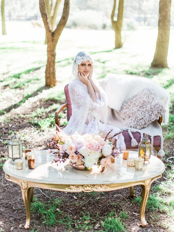 Bohemian bride with lace robe and veil sitting at table in woodland