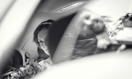 Bride sitting in back of wedding car with reflection of groom in window - Picture by Sean O'Dell Photography