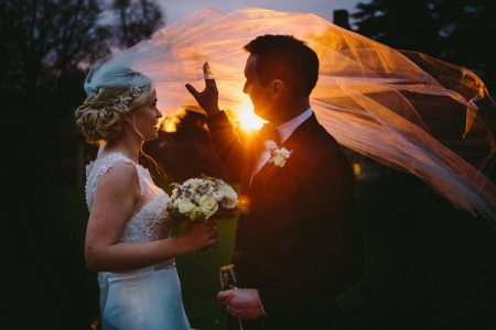 Groom holding up hand as sun shines through bride's veil - Picture by Kevin Belson Photography