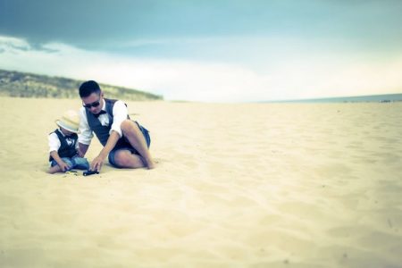 Groom sitting on beach with young pageboy in shorts and waistcoat - Picture by Thomas Frost Photography