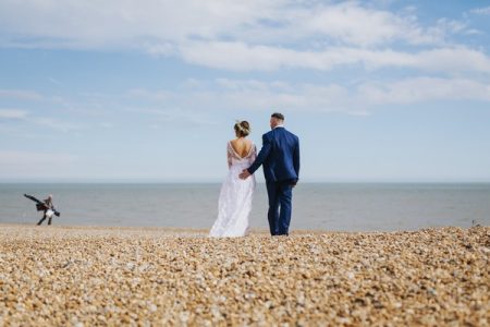 Bride and groom on the beach as fisherman walks past - Picture by Benjamin Stuart Photography