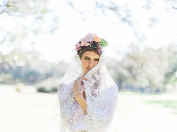 Bohemian bride with flower crown pulling lace veil over face