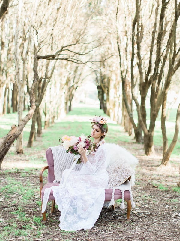 Bohemian bride sitting on couch in woodland