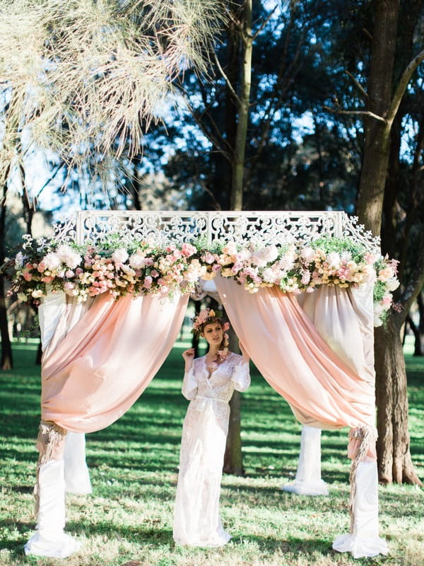 Bohemian bride under ceremony structure with flowers and drapes