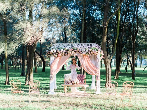 Bohemian bride standing under ceremony structure in woodland