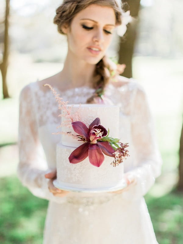 Bohemian bride holding wedding cake with large red flower