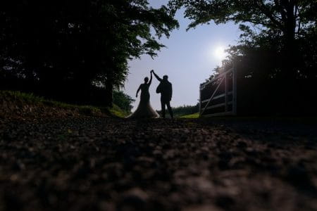 Groom holding up bride's arm as she twirls on country lane - Picture by Paul Keppel Photography