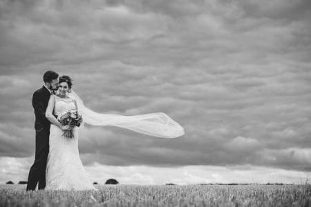 Bride and groom in field with bride's long veil blowing in wind - Picture by Gareth Newstead Photography