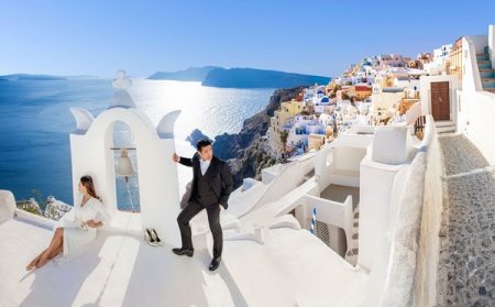 Bride and groom posing with Santorini in background - Picture by Clane Gessel Photography