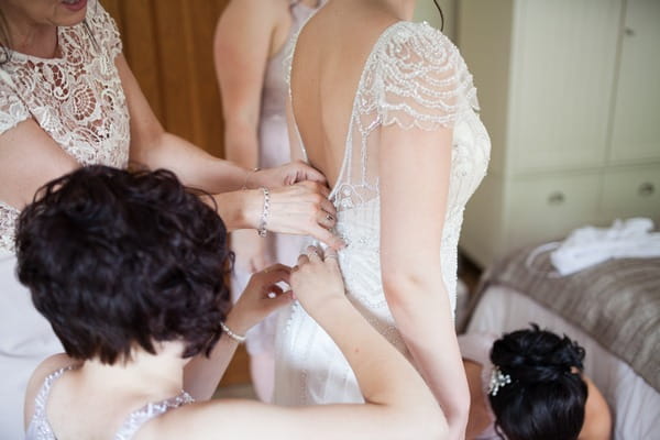 Bridesmaids doing up back of bride's dress