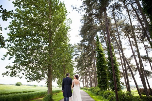 Bride and groom walking past trees at Packington Moor