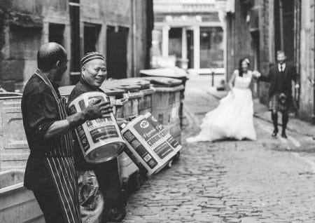 Men playing empty oil drums as bride and groom walk down cobbled street - Picture by Chris Scott Photography