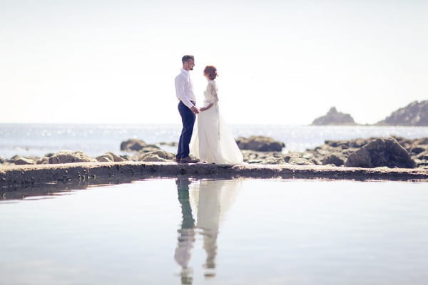 Bride and groom on rocks by sea in Cornwall