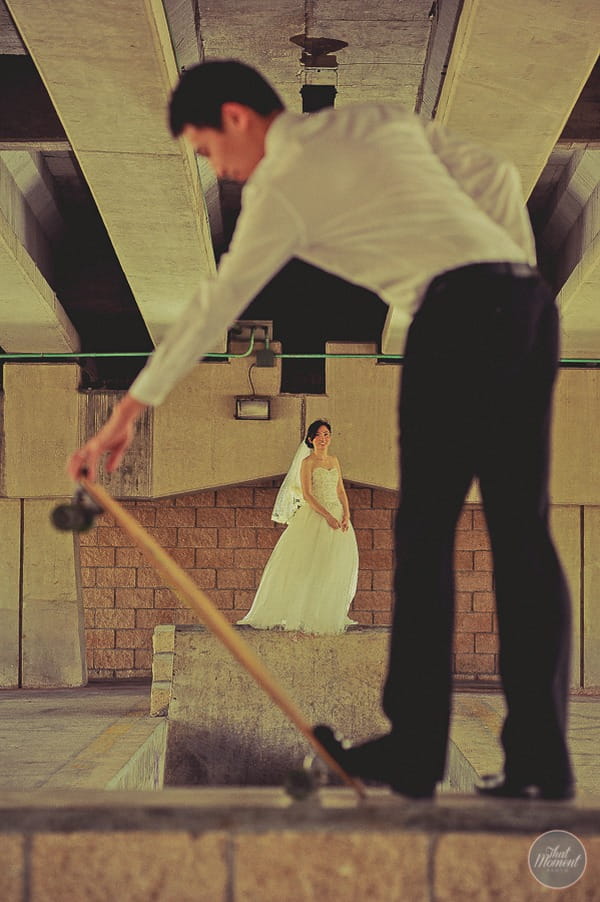 Groom flipping up skateboard as bride watches in background