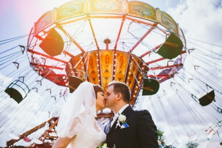 Bride and groom kissing under fairground ride - Picture by Clare Tam-Im Photography