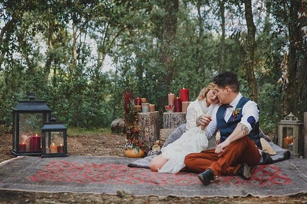 Bride and groom sitting on rug in woods