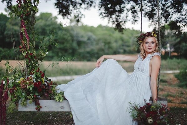 Boho bride sitting on swing with flowers