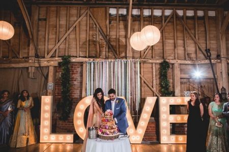 Couple cutting wedding cake with large illuminated letters behind them