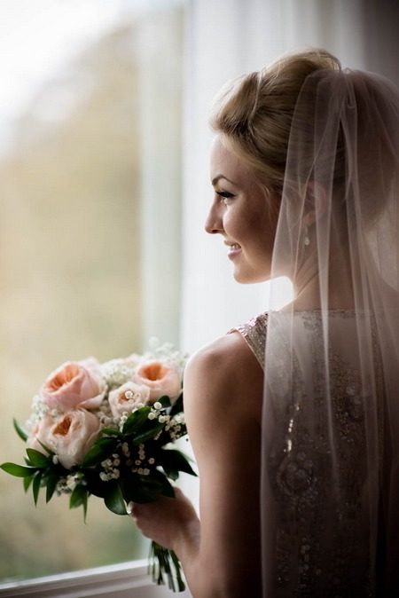 Smiling bride with bouquet looking out of window - Picture by Cassie Leedham Photography