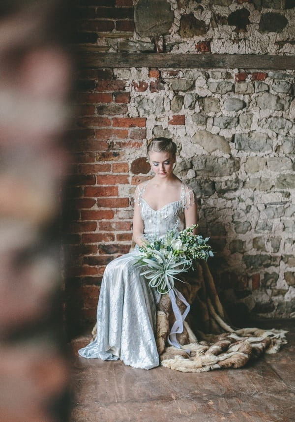 Bride sitting on chair looking down at bouquet