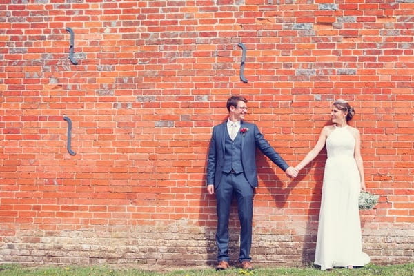 Bride and groom holding hands in front of wall