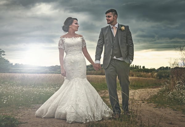 Bride and groom holding hands in field with black clouds overhead - Picture by Simon Emmett Photography