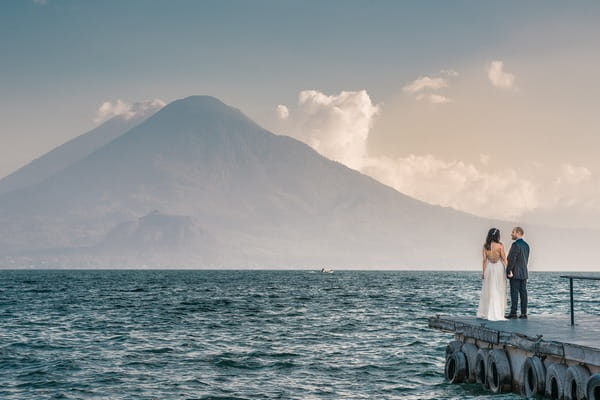 Bride and groom standing on jetty with sea and mountains in front of them - Picture by Daniel Lopez Perez