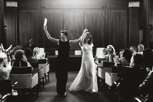 Delighted brides with arms in the air as they leave wedding ceremony - Picture by Lyndsey Goddard Photography