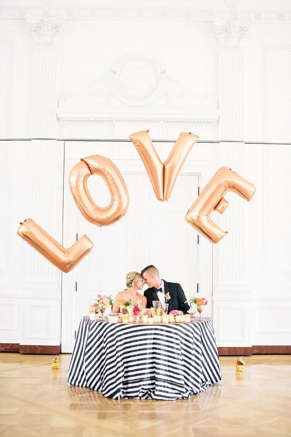 Bride and groom kissing behind LOVE letter balloons