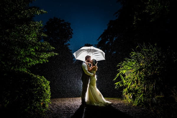 Bride and groom kissing under umbrella in rain - Picture by Libra Photographic