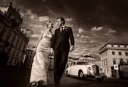 Bride and groom walking down road with wedding car behind - Picture by Matous Duchek