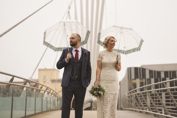 Bride and groom standing on a bridge holding umbrellas - Picture by Rebecca Parsons Photography