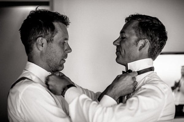 Grooms tying each others bow ties