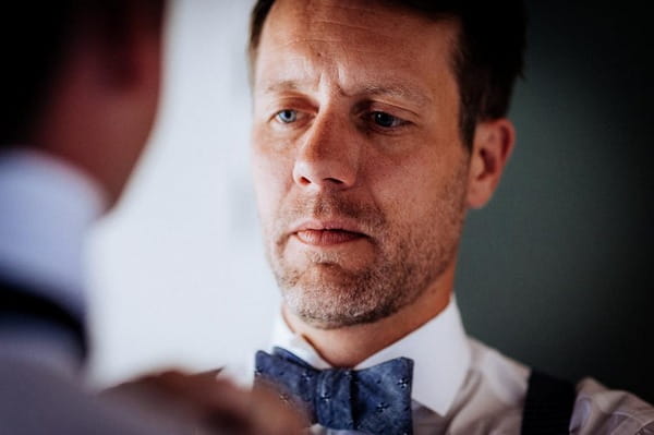 Groom concentrating as he ties bow tie