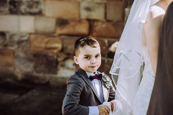 Young boy holding up bride's train on wedding dress