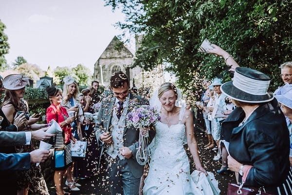 Bride and groom closing eyes as they walk through confetti shower