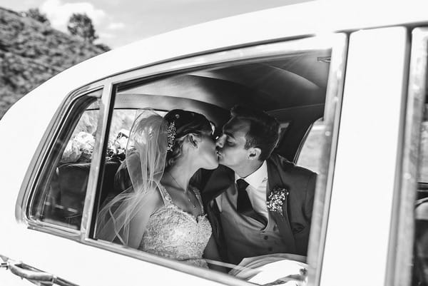 Bride and groom kiss in back of wedding car