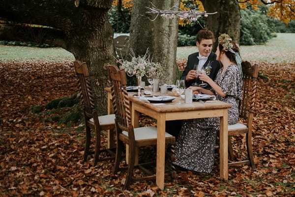 Bride and groom sitting at wedding table under tree